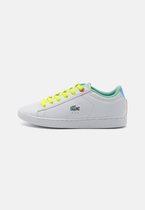 Baskets blanches avec lacets jaune néon, doublure intérieure vert menthe et petit logo crocodile vert brodé sur le côté.