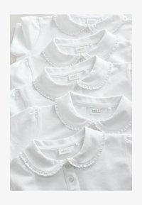 Cuatro camisas blancas con cuello y bordes rizados, apiladas ordenadamente, con cierres de botones y etiquetas visibles en los cuellos.