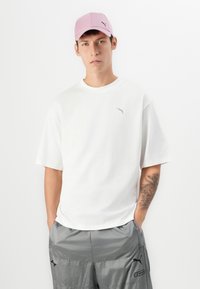 Bílý bavlněný tričko s malým šedým logem Puma, spárované se šedými sportovními šortkami s černými akcenty a růžovou kšiltovkou.