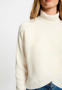 Maglione a dolcevita crema realizzato in tessuto a coste, con una vestibilità ampia e un design cropped. Abbinato a denim testurizzato.