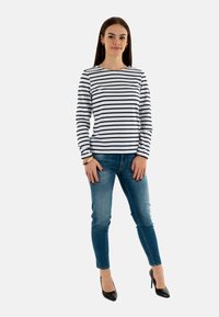 Maglietta a maniche lunghe a righe blu e bianche abbinata a jeans blu aderenti e tacchi alti neri. La maglietta ha un colletto rotondo e una vestibilità comoda.