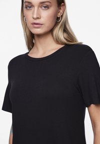 Must have lühikeste varrukatega must T-särk, mis on valmistatud pehmest kangast, klassikalise ümmarguse kaelusega. Sile tekstuur ja puhas, minimalistlik disain.