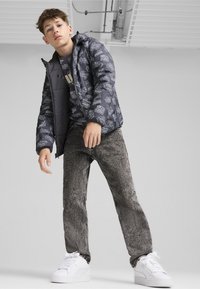 Grå puffjacka med grafiskt tryck, svarta jeans med en urtvättad textur och vita sneakers. Avslappnad klädsel, enkel design och monokroma färger.