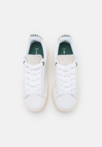 Sneakers bianche con una texture liscia, dettagli verdi sulla soletta e una linguetta color beige chiaro con il logo "LACOSTE". Design classico con lacci.