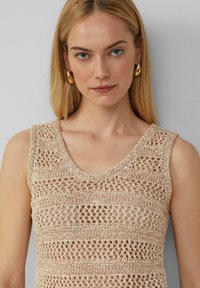 Gebreide mouwloze top in lichtbeige, met een textuurpatroon met opengewerkte strepen. Ronde halslijn, zacht materiaal en aansluitend ontwerp.
