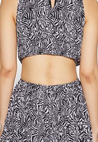 Μαύρο και λευκό cropped top με σχέδιο ζέβρας και λαιμόκοψη keyhole. Το ύφασμα είναι ελαφρύ και ελαφρώς υφαντό.