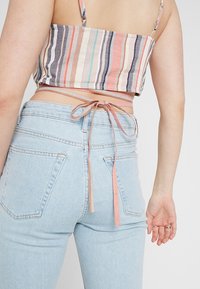 Randig kort topp med flerfärgade linjer; knuten i ryggen. Höga ljusblå jeans med en åtsittande design och två bakfickor.