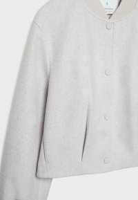 Veste en laine gris clair avec col côtelé, boutons-pression sur le devant et poches dans les coutures latérales, présentée sur fond blanc.
