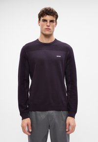 Dunkellila Pullover mit Rundhalsausschnitt, ausgestattet mit strukturierten Schulterakzenten und einem kleinen weißen "BOSS"-Logo auf der Brust. Gefertigt aus gestricktem Material.