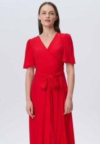 Rotes Wickelkleid mit kurzen Puffärmel, einem tiefen V-Ausschnitt und einem Bindegürtel. Der Stoff hat eine strukturierte Optik und ein fließendes Design.
