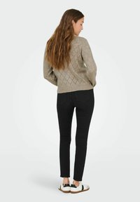 Ljusgrå, texturerad tröja med diamantmönster, kombinerad med svarta skinny jeans och vita sneakers med svarta detaljer.