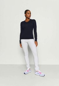 Top de manga larga en color navy, jeans ajustados blancos y zapatillas con detalles en rosa. El top presenta un diseño de escote en v, y el conjunto tiene un aspecto casual.