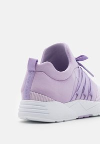 Fioletowe tekstylne sneakersy z plecionym wierzchem, wyściełanym kołnierzem oraz białą gumową podeszwą z geometrycznymi akcentami i pętlą na pięcie.