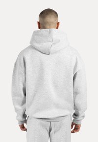 Sweatshirt gris en tissu doux, présentant une grande capuche et une coupe décontractée. L'arrière comporte des coutures marquantes et des poignets côtelés.