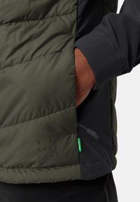 La giacca imbottita presenta un design verde scuro e nero, con una texture liscia, tasca laterale e cuciture con etichetta ecologica.