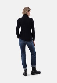 Schwarzer Rollkragenpullover, taillierte Passform, kombiniert mit blauen Jeans, gerader Schnitt, hochgerollte Säume und schwarzen Ankle Boots mit stabiler Sohle.