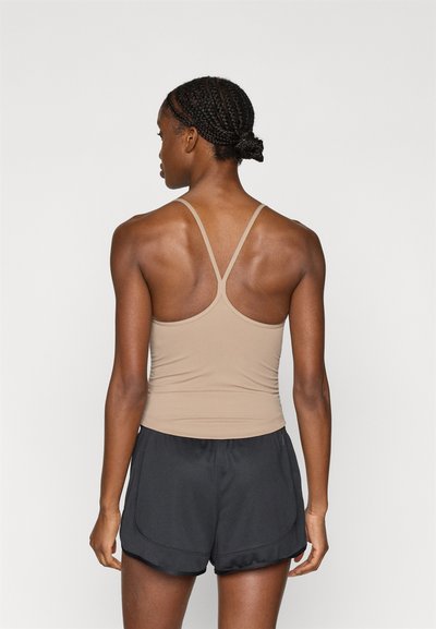 Top canottiera aderente color beige con spalline sottili e design a racerback, abbinato a pantaloncini sportivi neri con orlo curvo. Tessuto liscio ed elastico.