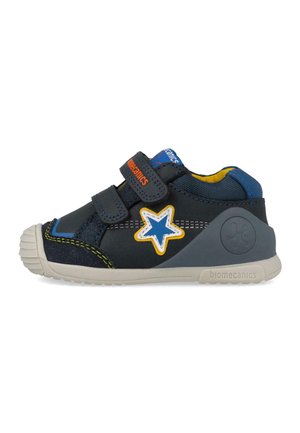 Zapatilla infantil azul marino con suela blanca, dos tiras de velcro, parche de estrella azul con contorno amarillo y soporte de talón gris.