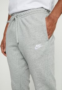 Grå Nike träningsbyxor med resårmidja och dragsko, med sidofickor och en liten vit logotyp på vänster lår.