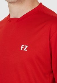 Rød atletisk skjorte med rund hals, lavet af glat stof. Har et hvidt "FZ" logo på venstre brystområde. Korte ærmer.