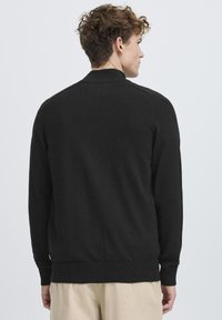 Cardigan nero a maglia con collo rotondo, polsini e bordo a coste. Presenta una texture liscia e un design semplice senza ulteriori motivi.