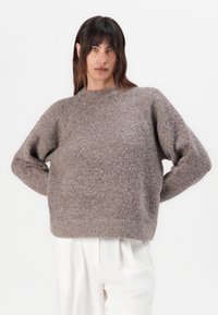 Pull en laine bouclée marron, avec un col rond et des manches longues ; coupe décontractée, tissu texturé ; assorti à un pantalon de couleur claire.