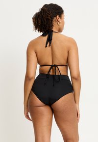 Ensemble de bikini noir comprenant un haut à col halter avec des liens et un bas taille haute. Tissu doux sans motifs ni accents visibles.