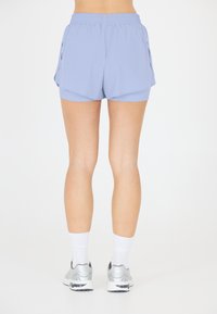 Valkoiset urheilushortsit, joissa on joustava vyötärö, kerroksellinen muotoilu ja kaksi sivutaskua. Yhdistettynä valkoisiin sukkiin ja hopeisiin lenkkareihin.