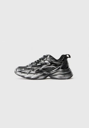 Black and silver athletic shoes with a mesh upper, curved sole, textured pattern, and lace-up closure. Features distinct layering and accents.