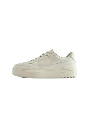 Baskets basses beige avec lacets à l'avant, semelle épaisse et design cousu discret sur le côté, vues de l'extérieur.