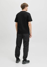 Sort bomulds t-shirt med rund hals, parret med løstsiddende sorte bukser med hvide sidestriber og sorte sportsko.