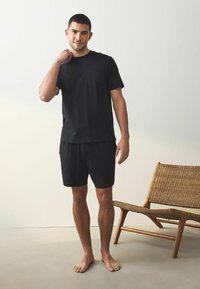 Tricou negru din bumbac cu mânecă scurtă, dotat cu un buzunar pe piept, asortat cu șorturi negre. Design simplu, croială casual, textură moale.