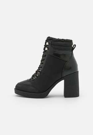Botines negros hasta el tobillo con acabado en charol, cordones delanteros, tacones gruesos con textura y un puño acolchado en el tobillo.