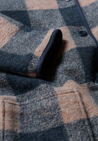 Villane särkjakk, millel on pruunide ja tumesiniste ruutude muster, tumesinine soonikkoes krae, ees nupud ja tekstureeritud kangas.