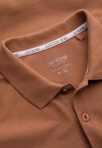 Brun bomullspolo skjorta med en strukturerad yta, med en nedvikt krage, två knappar och en etikett som säger "ombre cotton line".