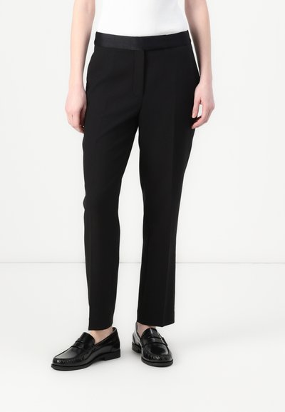 Sorte skræddersyede bukser med en glat talje, slim fit og diskrete frontfolder. Båret med sorte loafers og en tætsiddende hvid top.