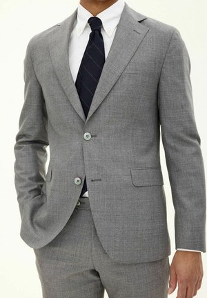 Grau Anzugsjacke aus einem strukturierten Stoff, mit zwei Knöpfen, Reverskragen und Seitentaschen. Kombiniert mit einem weißen Hemd und einer dunkel gestreiften Krawatte.