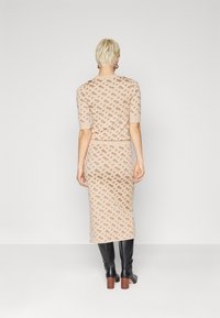 Abito in maglia color beige chiaro con un motivo geometrico ripetuto in marrone. Presenta maniche corte e una silhouette aderente, abbinato a stivali neri al ginocchio.