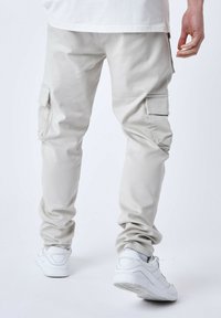 Pantaloni cargo grigi chiari con multiple tasche laterali, polsini elasticizzati e una texture morbida. Abbinati a sneakers bianche, mostrati da dietro.