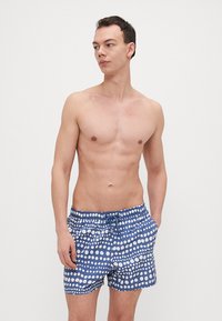 Blå shorts med hvite prikker, med elastisk midje og sidelommer. Glatt stofftekstur.