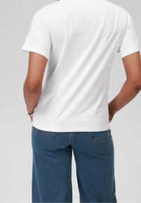 Bílý bavlněný tričko s krátkými rukávy, s rovný střih a hladkou texturou. Nosené s modrými džínovými kalhotami se širokými nohavicemi.