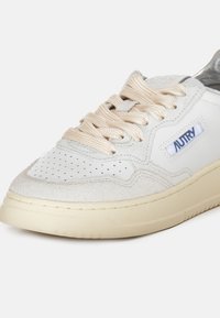 Sneaker bianco con tomaia in suede beige e pelle liscia, punta forata, lacci beige e suola in gomma crema. Presenta il logo 'AUTRY' sul lato.