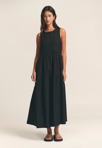 Čierna, bezrukávová maxi šaty s okrúhlym výstrihom, vrstveným dizajnom a voľnou sukňou. Hladká tkanina s uvoľneným strihom. Jednoduchý, elegantný dizajn.