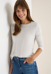 Maglione grigio chiaro a maniche lunghe con scollo rotondo, abbinato a jeans in denim blu. Il materiale sembra morbido con una trama sottile.