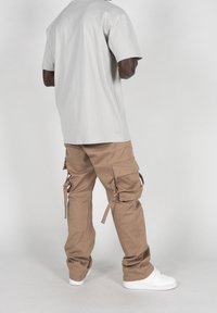 Camiseta de algodón gris y pantalones cargo marrones con múltiples bolsillos y cordones, combinados con zapatillas blancas. Diseño y ajuste simples y casuales.