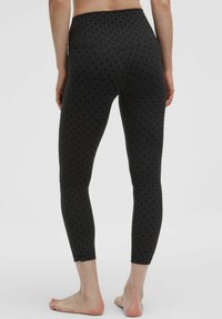 Fekete leggings pöttyös mintával, magas derekú kialakítással, sima textúrával és rövidített hosszal, diszkrét logóval a szegély közelében.
