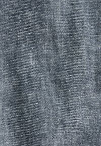 Tume sinine denimpool, mis on sileda tekstuuriga, delikaatse kootud mustriga ja kerge kulumisega, sobilik rõivaste valmistamiseks.