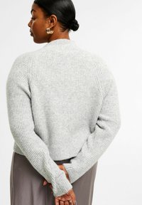 Grå ribbad tröja med hög krage och långa ärmar, med en avslappnad passform och en något croppad nederkant. Minimalistisk design.