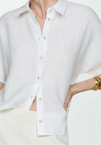 White linen shirt with a collar and short sleeves, featuring beige buttons down the front and a loose, relaxed fit.