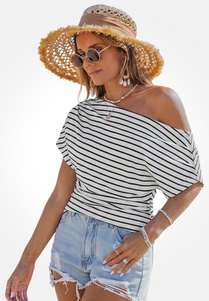 Kobieta ubrana w pasekowany top z odkrytymi ramionami, podarte szorty jeansowe, słomkowy kapelusz przeciwsłoneczny, okrągłe okulary przeciwsłoneczne, kolczyki z muszli oraz warstwowe bransoletki i naszyjniki.